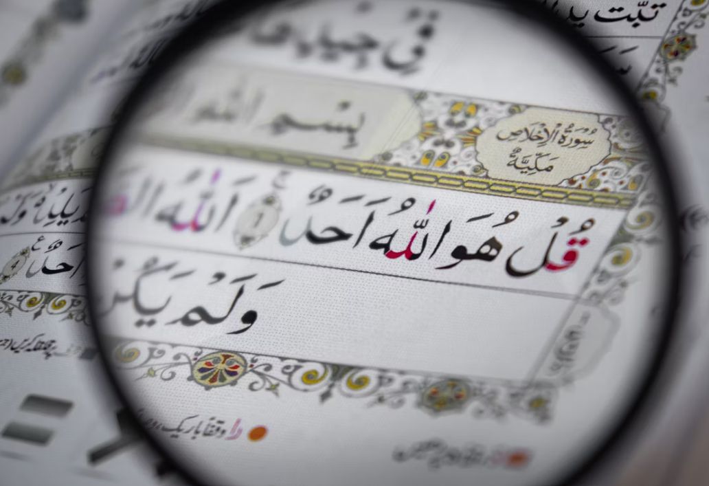 A magnifying glass over Surah Al-Ikhlas showing Tajweed detail